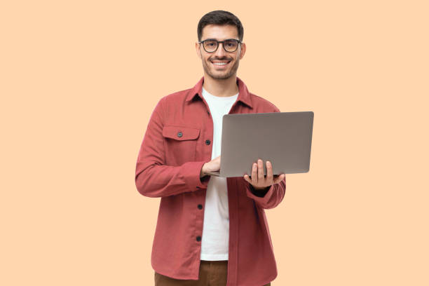 jovem em pé segurando laptop e olhando para a câmera com sorriso feliz - isolado - fotografias e filmes do acervo