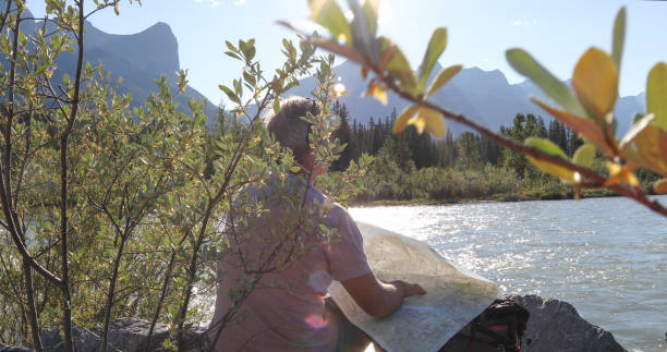 istock Hiker relaxes by riverside and checks map for direction 1326856776