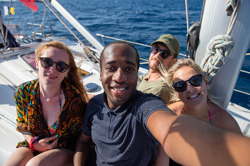 Multiethnic group of smiling people in a boat taking a selfie. Summertime picture, leisure and carefree concept.