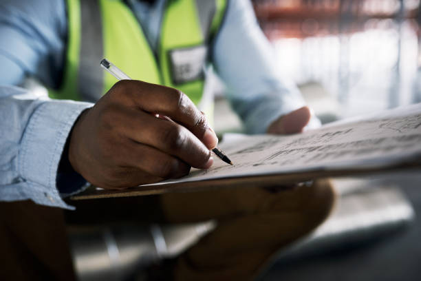 schuss eines nicht wiederzuerkennenden baumeisters beim ausfüllen von papierkram auf einer baustelle - building activity construction manual worker men stock-fotos und bilder