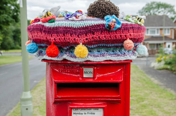 Crocheted and Knitted decoration on pillar box Basingstoke, UK - July 3, 2021: A crochet and knitted woollen decoration on top of a traditional red pillar box in Basingstoke, Hampshire.  The yarn bombing has brought smiles to those passing in Brighton Hill. basingstoke photos stock pictures, royalty-free photos & images