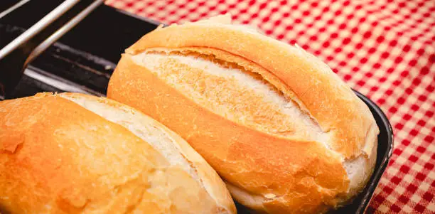 Photo of French bread. Two French buns served in a black baking dish on a table with a red checkered tablecloth.