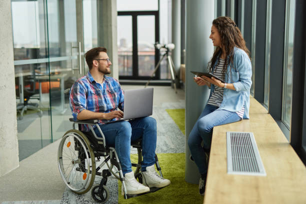 istock Disabled male computer programmer discussing with female coworker in office hallway 1326880681