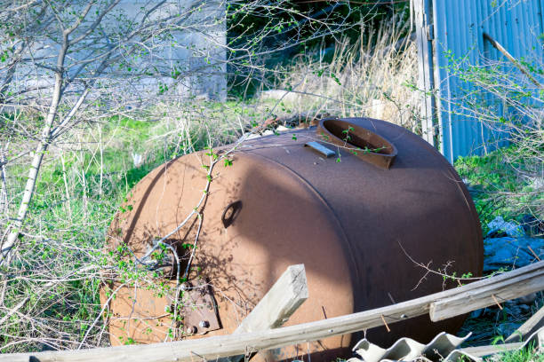 An old rusty metal tank to transport water. Lying in the grass next to the garbage.