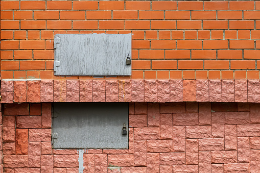 Two metal rectangular hatches in a red brick wall. Gray. Closed to locks.