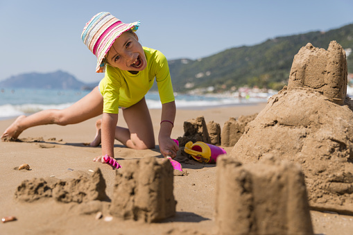 Happy young girl making funny faces when playing with toys in the sand