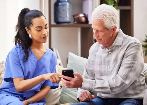 Photo of Shot of a young woman helping her elderly patient use a smartphone