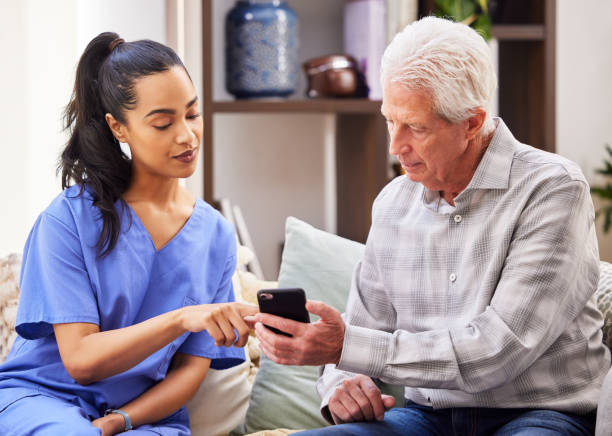 shot of a young woman helping her elderly patient use a smartphone - nurse on phone serious bildbanksfoton och bilder