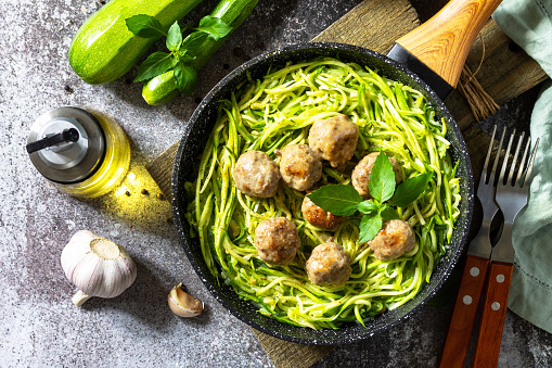 Healthy food, keto diet, lunch. Cooked zucchini noodles with meatballs on a stone countertop. Top view flat lay background.