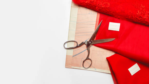 istock Tailor's desk. Pattern of clothes and sewing tools. Red satin, tulle, guipure fabric, scissors on a white table background. Space for text 1326894837