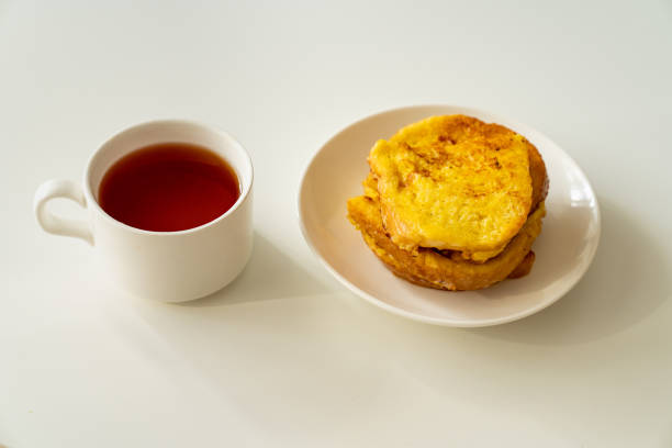 a cup of tea and croutons of bread and egg in a plate on a white table.