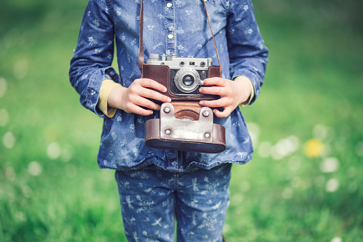 Little girl with old vintage camera making photos of surrounding nature in the park