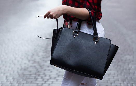 Closeup shot of woman holding big black leather purse. Space for text