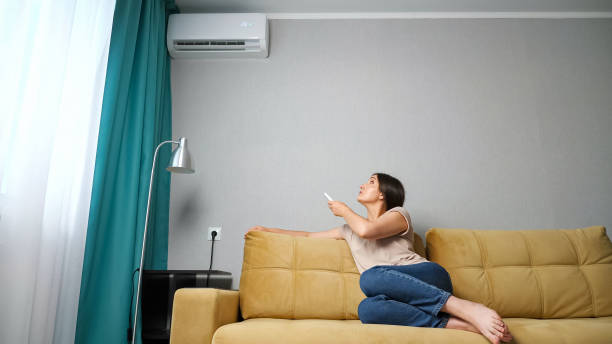 istock woman adjusts the air conditioner while sitting on the couch 1326917265