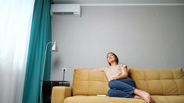 istock woman adjusts the air conditioner while sitting on the couch, 1326917266
