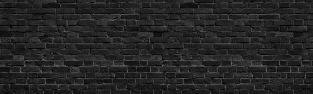 istock Old black shabby brick wall wide panoramic texture. Dark grey rough masonry. Aged brickwork panorama. Abstract grunge background 1326917283