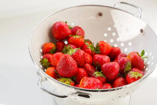 Fresh red ripe organic strawberry in the white steel colander. Healthy vegan food.