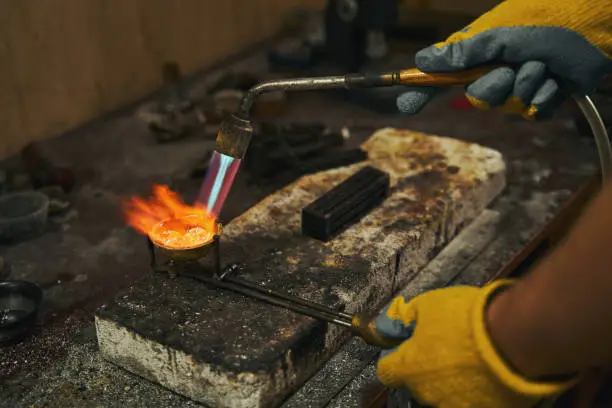 Jewelry maker melting substance for new product with fire from gas soldering torch on working table