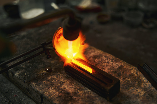 Jeweler turning over smelted steel from a crucible into casting form while creating a jewelry item