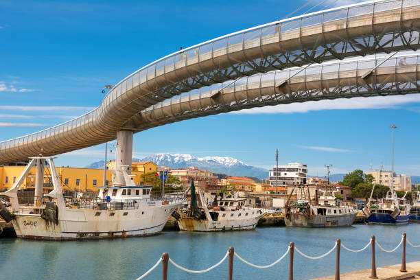 ponte del mare (seebrücke) und boote im hafen im kanal des flusses pescara und des majella-gebirges im hintergrund verankert - pescara stock-fotos und bilder