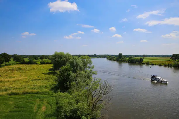 Panoramic view on typical dutch rural landscape with river maas and green agricultural fields in summer against blue sky near town Well