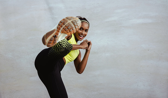 African woman in fitness outfit doing kick boxing workout. Athlete woman doing leg exercise against white background.