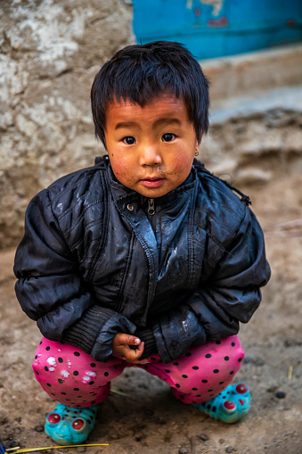 Tibetan little girl sitting next to her parents house, small village in Upper Mustang. Mustang region is the former Kingdom of Lo and now part of Nepal,  in the north-central part of that country, bordering the People's Republic of China on the Tibetan plateau between the Nepalese provinces of Dolpo and Manang.