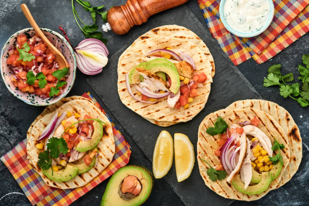 istock Mexican tacos with grilled chicken, avocado, corn kernels, tomato, onion, cilantro and salsa at black stone table. Traditional Mexican and Latin american street food. Top view. 1326934943