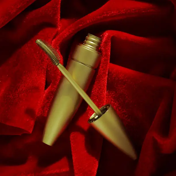 Photo of Gold mascara on red velvet. Promotional photo of cosmetics. top view