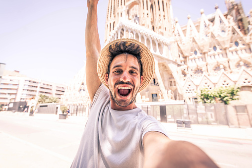 Happy tourist visiting La Sagrada Familia, Barcelona Spain - Smiling man taking a selfie outdoor on city street - Tourism and vacations concept