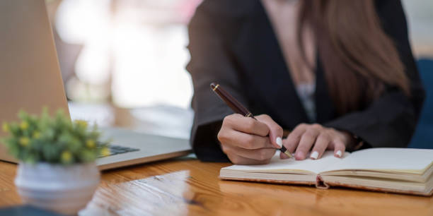 istock Close up woman's hands with laptop computer, notebook and pen taking notes in business office 1326940088