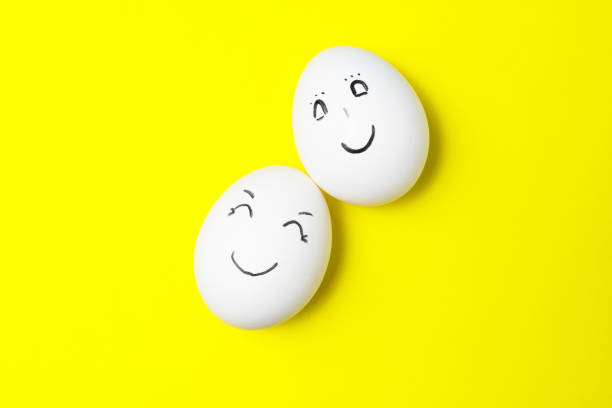 istock Two white chicken eggs with smiling faces on yellow background. 1326943332