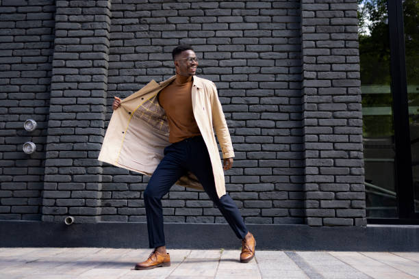Handsome African American male model posing on the city street Attractive and handsome African American male model wearing a fashionable coat posing while standing on a city street and smiling street fashion stock pictures, royalty-free photos & images
