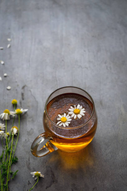 té de manzanilla en una taza de vidrio en una mesa rústica - manzanilla fotografías e imágenes de stock