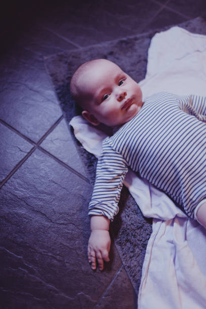baby lies on a rug in the bathroom on a warm floor stock photo