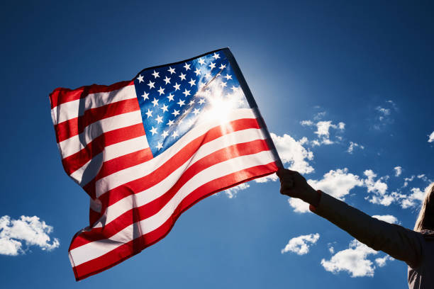 istock Waving usa flag in hand against blue sky 1326952613