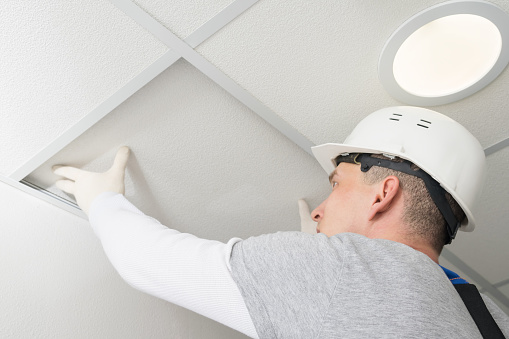 a worker in a helmet installs the last piece of the false ceiling