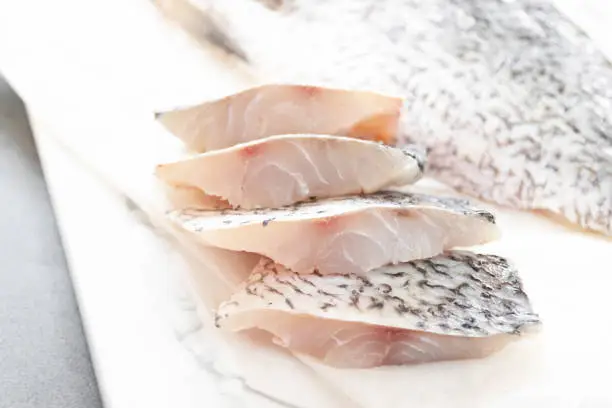 Photo of Fresh sea bass fish fillets on marble cutting board; selective focus.
