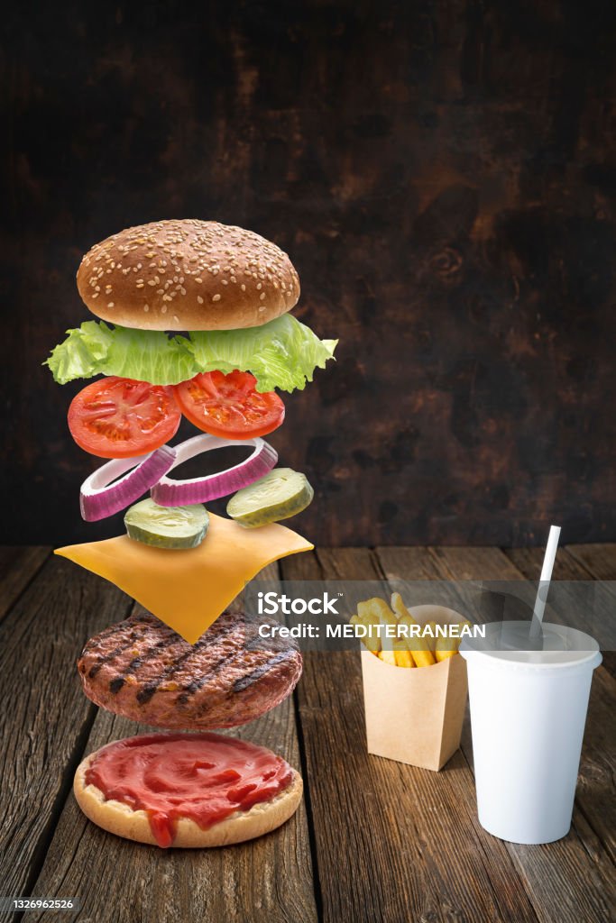 Burger ingredients flying with combo of french fries and disposable beverage paper glass on dark wood Burger ingredients flying with combo of french fries and disposable beverage paper glass on dark wood background Food Stock Photo