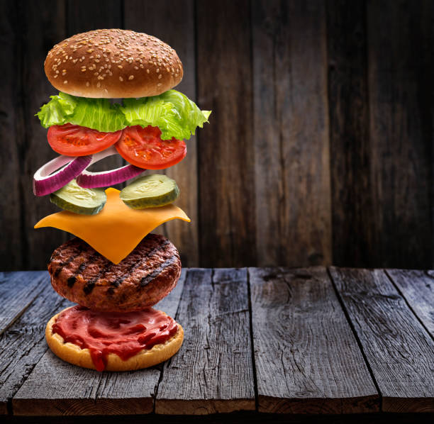istock Burger layered ingredients as explosion flying open bun on rustic wooden table 1326962601