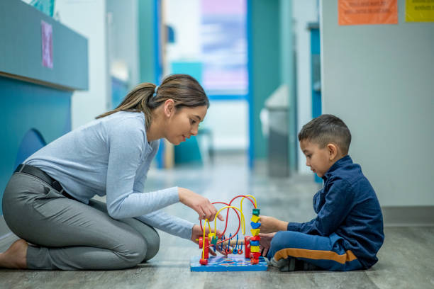 Female occupational therapist and young child patient A young female occupational therapist is seated across a young male patient. They are both focused on playing with a bead maze that is in between them. They are both dressed casually for their appointment together. occupational therapy photos stock pictures, royalty-free photos & images
