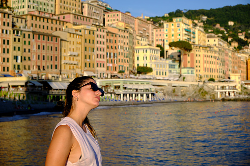 a young model wearing sunglasses in the coast a the beach of camogli, Liguria, Italy. with the colorful houses at the background