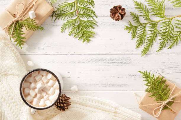 istock fir branches, thuja twigs, fir cones, gift box, hot chocolate mug with marshmallows, white sweater on a white wooden background, place for the inscription 1326972422