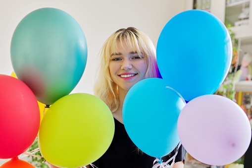 Close up of colored balloons and happy smiling face of blonde teen female. Birthday 16, 17 years, holiday, happiness, joy, bright balloons background