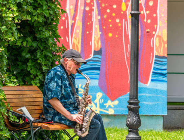 musicista di street artist senior seduto su una panchina nel parco e che suona al sassofono - romania men artist portrait foto e immagini stock