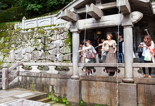 Kyoto, Japan - July 18, 2011: Visitors catch water from a sacred waterfall at the Kiyomizu-dera temple using the buckets with a long handle