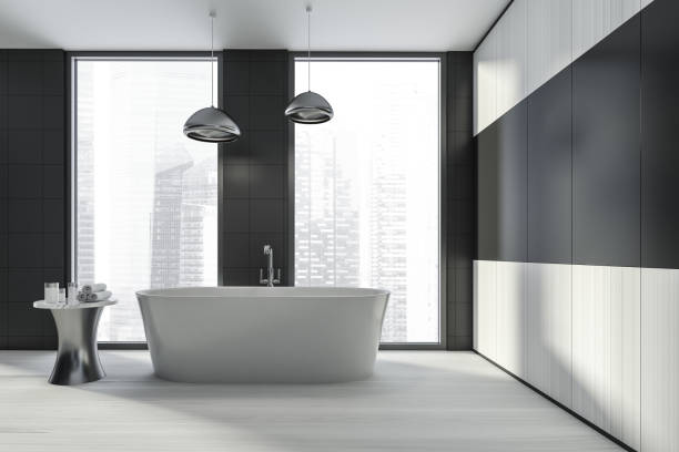 istock Modern design bathroom interior with white oval bathtub, silver faucet, lamp. Small table with towel and cosmetics. Panoramic window with skyscrapers city view. Wood materials. 1326977100