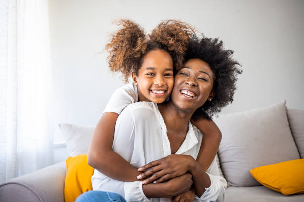 donna e bambina attraenti sedute sul comodo divano di casa. - family african descent cheerful happiness foto e immagini stock