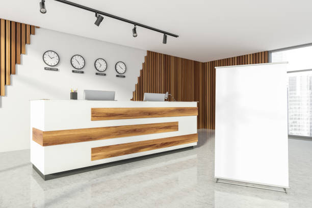 istock Empty office, wooden reception interior at white wall, 4 clocks on it. Panoramic window. Hotel check in desk. Blank roll-up banner. 1326979411