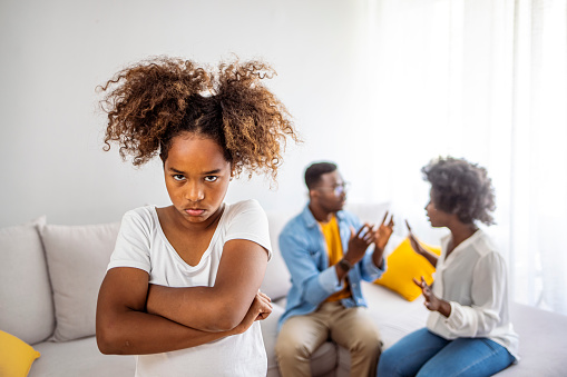 Sad girl listening to her parents arguing in the living room. Sad little girl and family fight in living room. Kid daughter feels upset while parents fighting at background